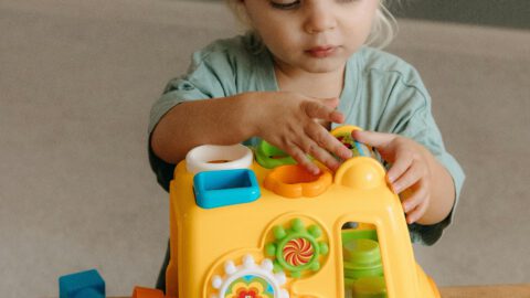 Cute toddler engaging with colorful toy bus inside a playroom.