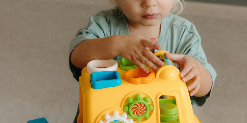 Cute toddler engaging with colorful toy bus inside a playroom.