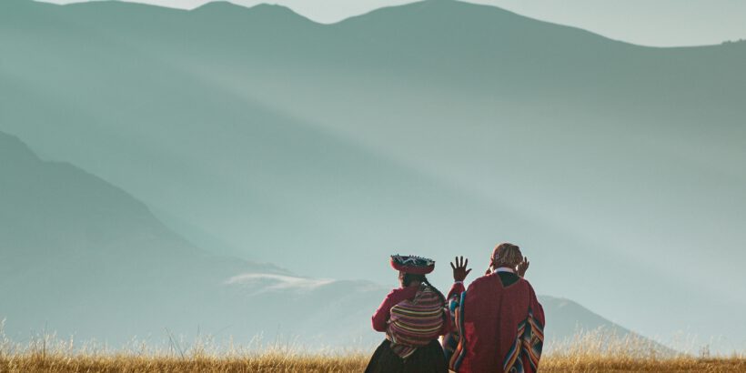 Two people in traditional Andean clothing sit in the mountains of Cusco, Peru.